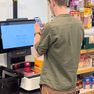 Man using smartphone at a Scandit self-checkout kiosk in a grocery store, with shelves of snacks and a shopping basket nearby.