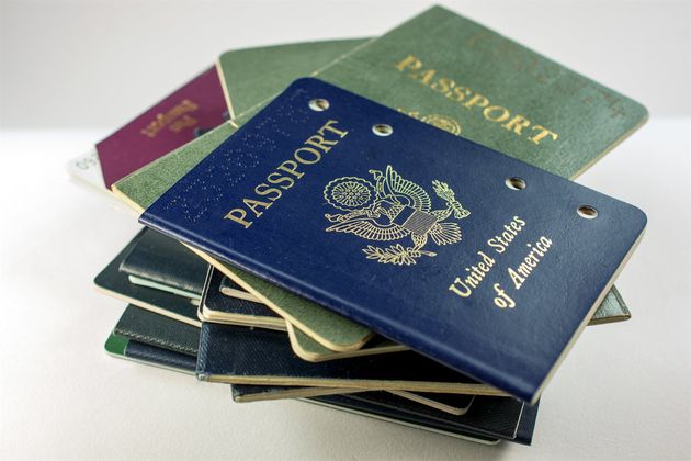 A stack of various passports, with a blue United States passport prominently on top, displaying the seal and text "United States of America."