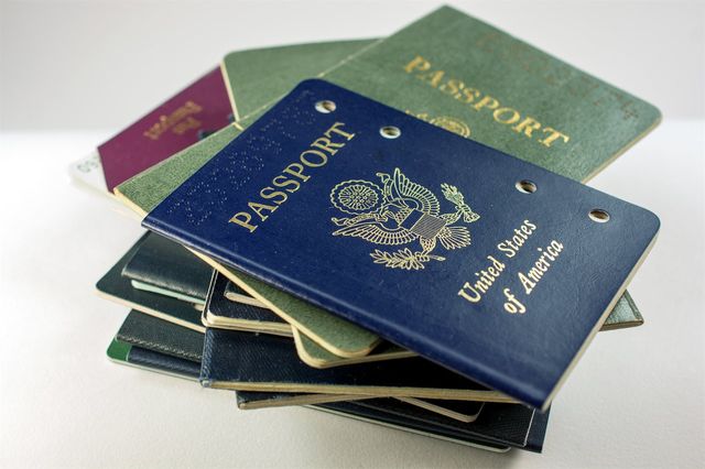 A stack of various passports, with a blue United States passport prominently on top, displaying the seal and text "United States of America."