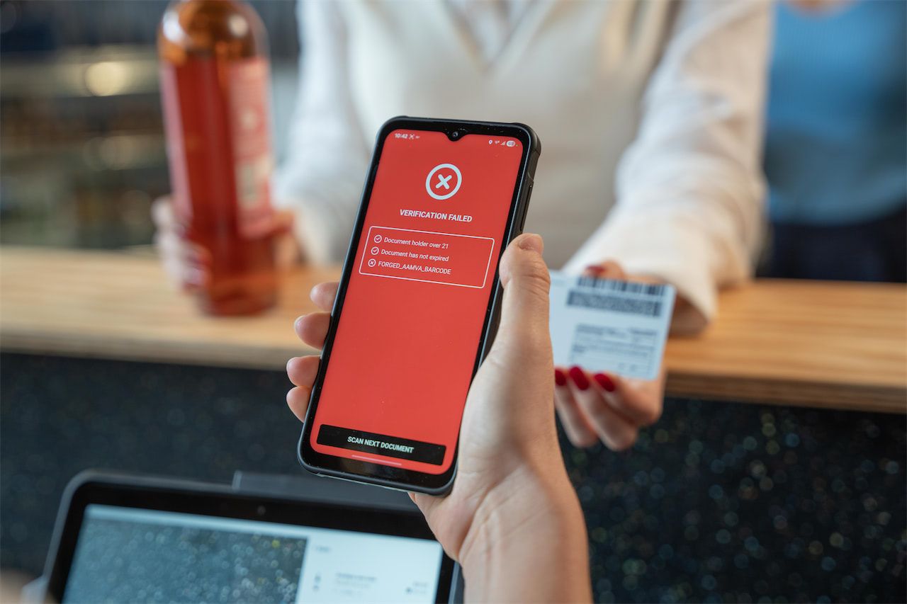 Person holding a phone displaying "Verification Failed" screen, while another holds a bottle and ID card at a counter.